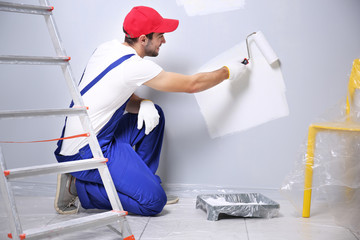Young worker painting wall in room