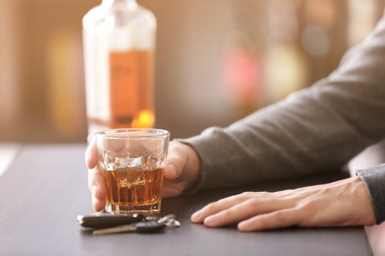 Man sitting in bar with car key and glass of alcoholic beverage, closeup. Don't drink and drive concept