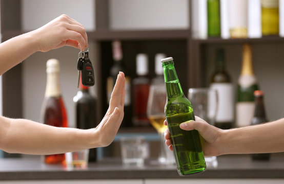 Woman with car key refusing bottle of beer, on blurred background. Don't drink and drive concept