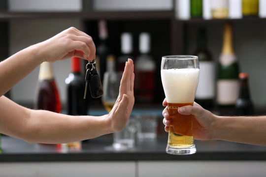 Woman with car key refusing glass of beer, on blurred background. Don't drink and drive concept