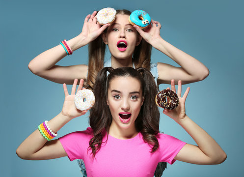 Funny young women with tasty donuts on color background