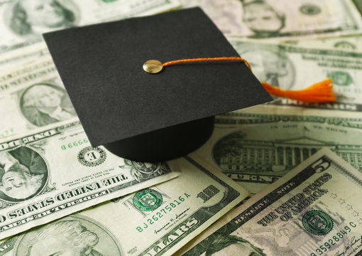 Close up view of graduation hat on dollar banknotes. Tuition fees concept