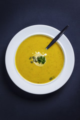 Pumpkin soup with cream, seeds and parsley served in a white pla