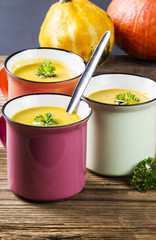 Pumpkin soup in colorful enamel mugs with seeds and parsley