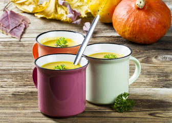 Pumpkin soup in colorful enamel mugs with seeds and parsley