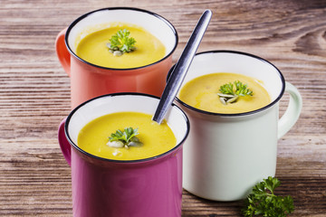 pumpkin soup in colorful enamel mugs with seeds and parsley