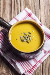 Pumpkin soup in a brown, ceramic bowl on a wooden table