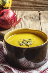 Pumpkin soup in a brown, ceramic bowl on a wooden table
