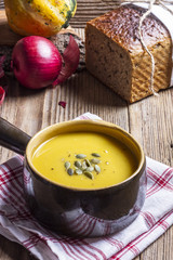Pumpkin soup in a brown, ceramic bowl on a wooden table