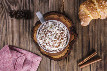 Hot cocoa with whipped cream, a bun and cinnamon on a wooden tab