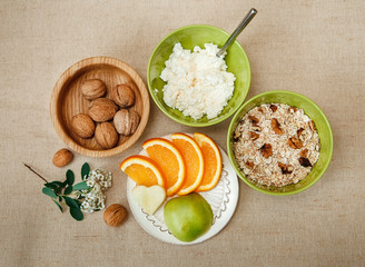 Table Appointments for Healthy Organic Breakfast.Walnuts,Oatmeal and Cottage Cheese.Cut Orange and Apple.Green Ceramic and Wooden Plates with Flowers.