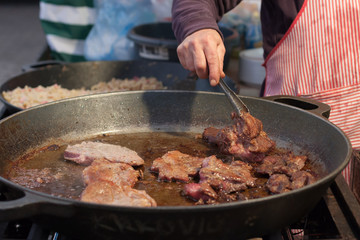 Man prepares fried meat in a pan at Christmas market