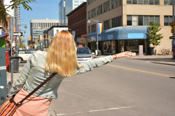 Young blonde lady is calling a taxi on the street.