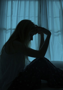 Silhouette of woman sitting in bed by window