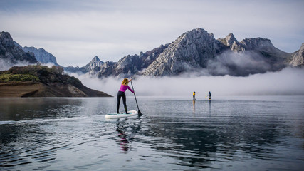 Naklejka premium A group of people paddle surfing on a lake with fog and mountains