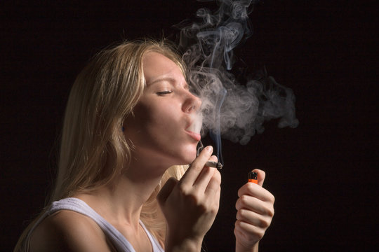 blond young woman smoking on black background