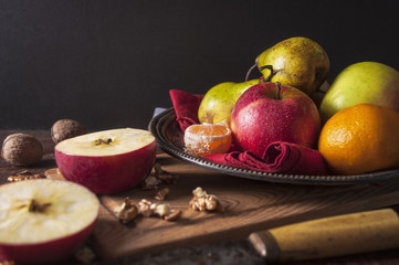 Pears, apples, walnuts and mandarines on plate on wooden table