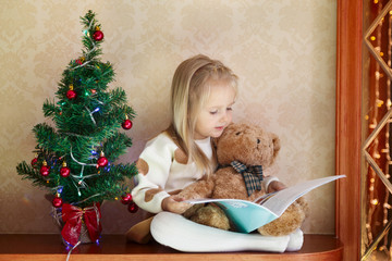a little girl sitting at home near the Christmas tree and reads a children's winter wonderland,...