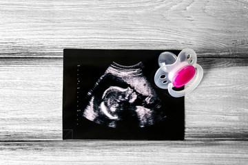 Ultrasound photo and pacifier on grey wooden background