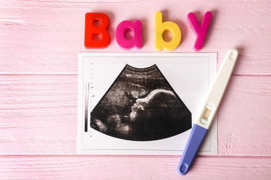 Ultrasound photo and pregnancy test on wooden background