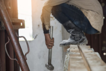 Worker wearing blue jeans and boots, holding a hammer on the scaffold,in construction site (focus at bar steel )