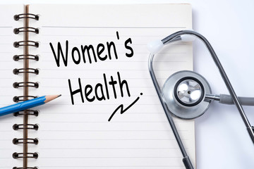 Stethoscope on notebook and pencil with women's health words as