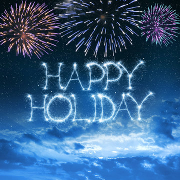 Happy Holiday written with sparkler on night sky with fireworks.