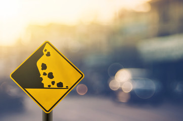 Falling stone warning traffic sign on blur road with colorful bokeh light abstract background.