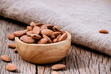 Closeup almonds kernels in wooden bowl with hemp sack on rustic