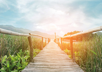 bamboo bridge walkway to lake on green field with burst sunrise
