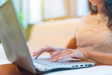 Fototapeta premium Female hands typing on keyboard. Cropped photo of a young woman holding laptop her knees and working.