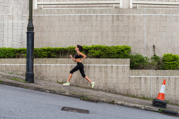Female runner running uphill on town street. Sporty young woman doing cardio exercises outdoors.