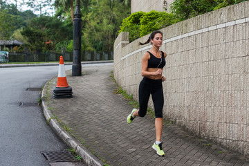 Fit young female jogger jogging on sidewalk in suburban area. Pretty girl working out outdoors.