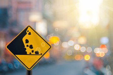 Falling stone warning traffic sign on blur road with colorful bokeh light abstract background.