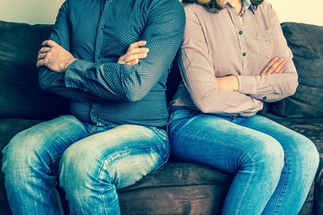 Displeased couple sitting back to back on couch - obrazy, fototapety, plakaty