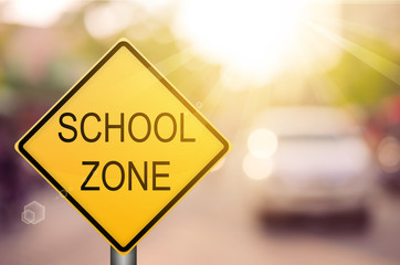 School zone warning sign on blur traffic road with colorful bokeh light abstract background.