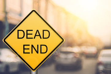 Dead end warning sign on blur traffic road with colorful bokeh light abstract background.