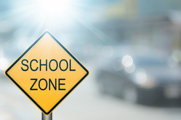 School zone warning sign on blur traffic road with colorful bokeh light abstract background.
