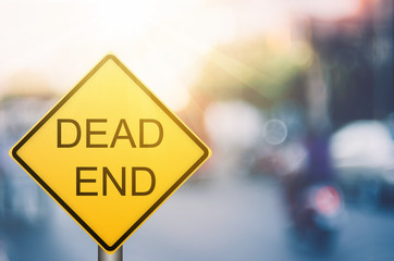 Dead end warning sign on blur traffic road with colorful bokeh light abstract background.