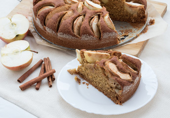 Vegetarian apple cake on a table with apple cut and cinnamon sticks