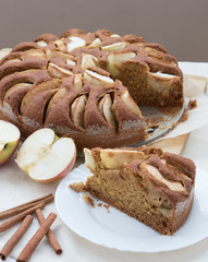 Vegetarian apple cake on a table with apple cut and cinnamon sticks