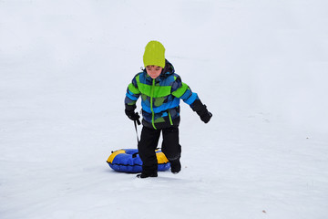 Fototapeta na wymiar European boy tugs at the inflatable slide (snow) sledge