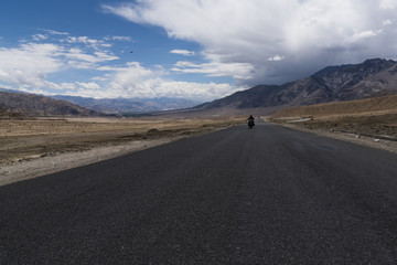 Motorcycle moving on a straight road in desert plains of Ladakh, with Himalayan mountains in the background. Ladakh is a cold desert in Tibetan plateau.