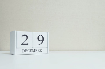 Closeup white wooden calendar with black 29 december word on blurred white wood desk and cream color wallpaper in room textured background with copy space , selective focus at the calendar