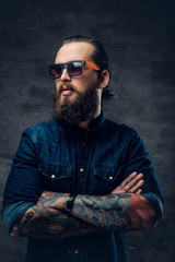 Bearded male in sunglasses with tattooed crossed arms.