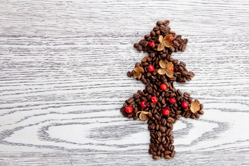 Christmas tree made of coffee beans decorated with red wild rose berries and dry flowers on wooden board floor background.  Winter and new year theme.