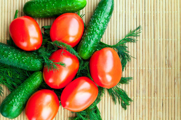 Red tomatoes, green cucumbers and greengrocery for salad on bamboo napkin.
