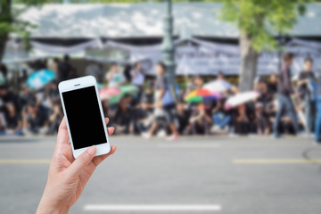 Woman hand holding and using mobile,cell phone,smart phone with isolated screen with blur image of people for background.
