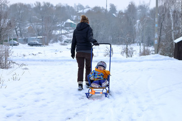 Fototapeta na wymiar Family fun, mother with her son on a sled on a winter day rolls down the hill