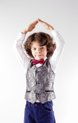 Curly cute boy in waistcoat and bow tie shows hands shelter. Close-up. Gray background.